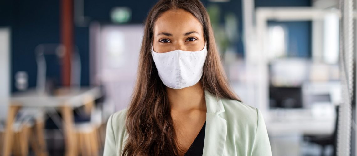 Close-up portrait of a businesswoman with face mask in office. Woman with protective face mask standing in office and looking at camera.