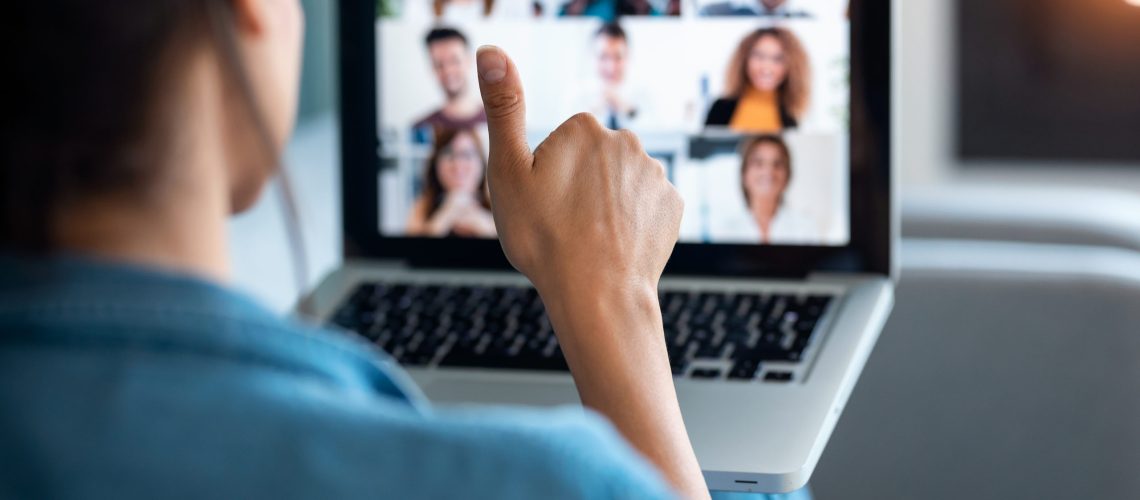 Back view of business woman making video call and showing thumb up to laptop on the online briefing while sit on sofa at home.